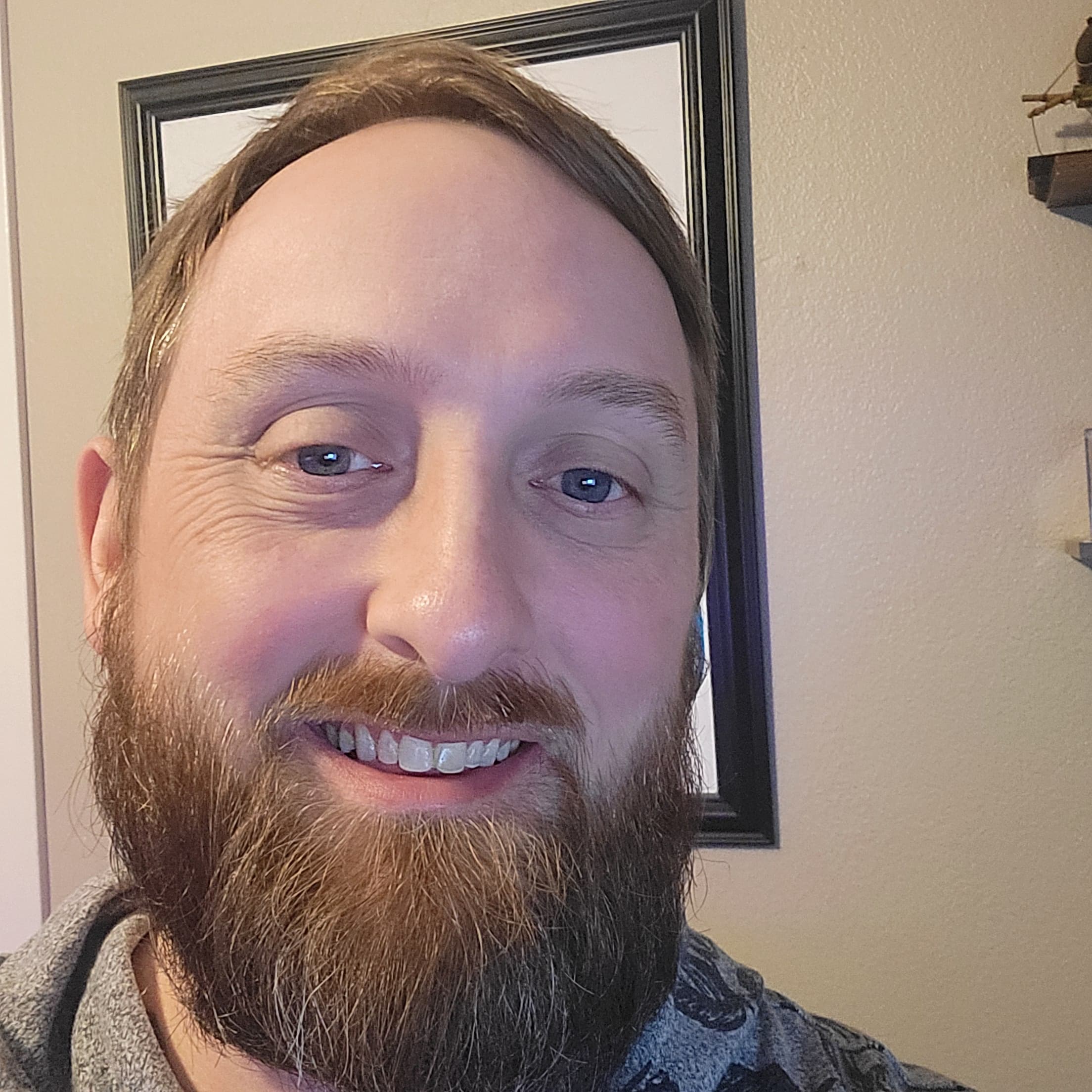 A smiling man with a full brown beard and blue eyes in a close-up.